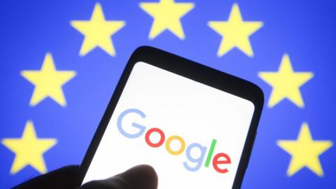 Google logo displayed on a phone in front of the EU flag - yellow stars on a blue background.