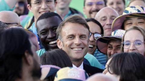 French President Emmanuel Macron poses with volunteers as he visits archery competitions during the Paris 2024 Olympic Games at the Esplanade des Invalides in Paris on August 2, 2024