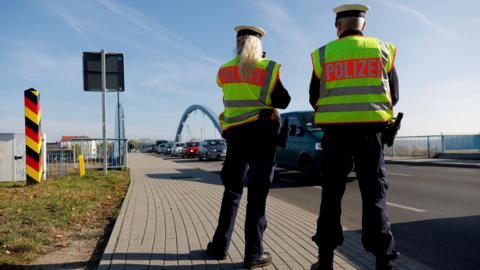 Two German federal police officers patrol a line of cars along the German-Polish border area in order to detain migrants from Belarus in 2021