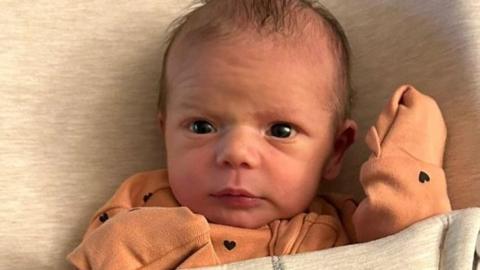 Baby in a little orange suit gazing up at camera