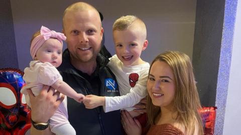 The Geddes family standing holding their children