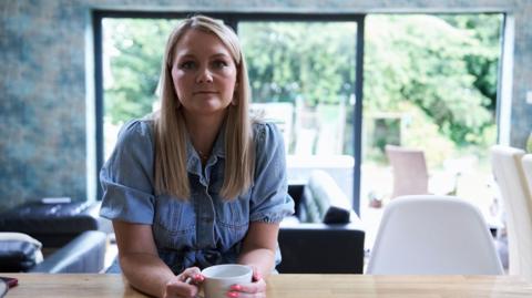 A blonde-haired woman sitting at a table drinking tea