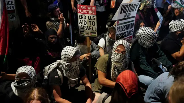 Pro-Palestinian demonstrators holding placards sit a street on the sidelines of the DNC.