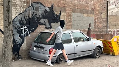 Person with balaclava walking away after defacing Banksy mural