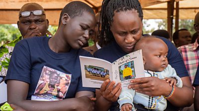 Mourners read the order of service at Rebecca Cheptegei's funeral. One of the two women holds a baby