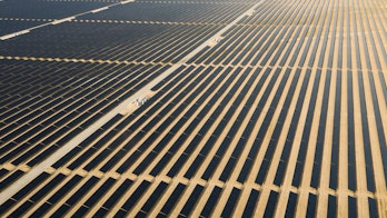 Photo depicts an Aerial view of a landscape with photovoltaic solar panel farm producing sustainable renewable energy in a desert power plant.