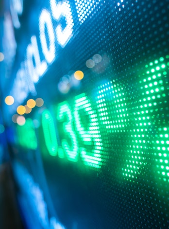 The photo depicts a display stock market numbers with defocused street lights background