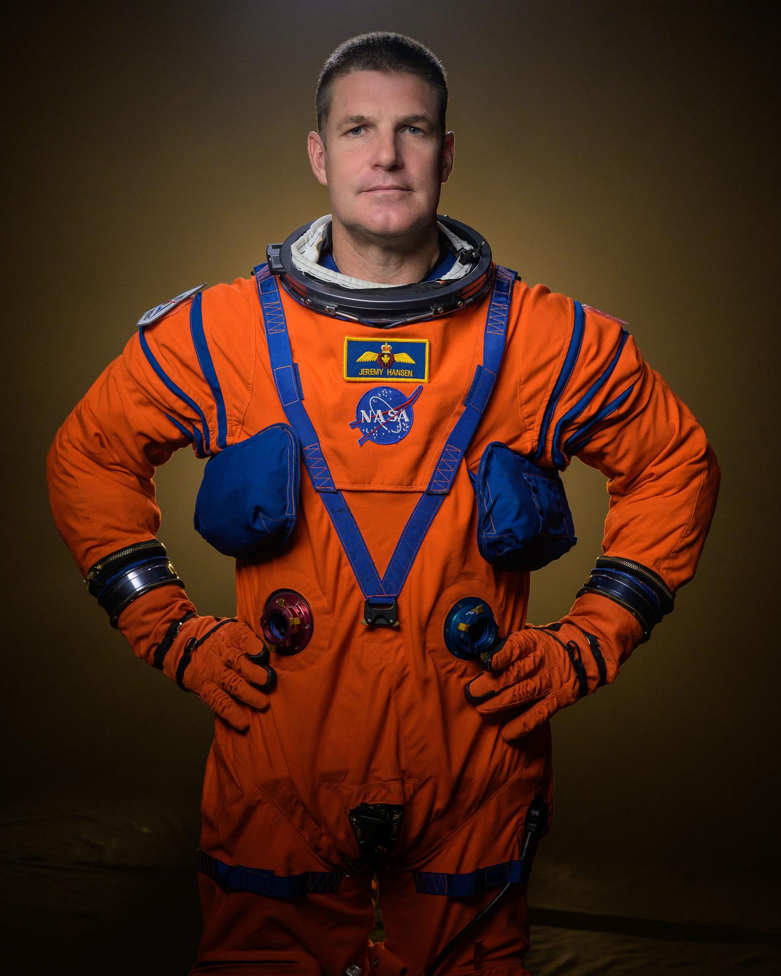 A man in an orange spacesuit with his hands on his hips.