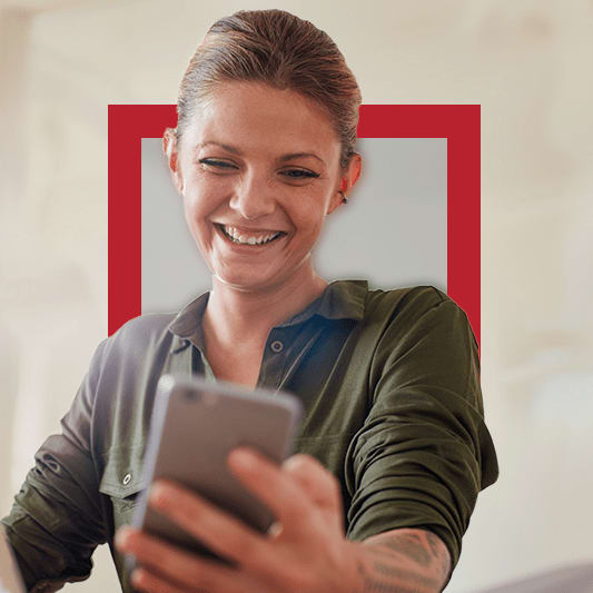 A woman sitting down and smiling while looking at her mobile device