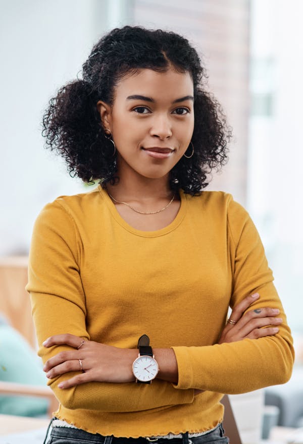 A young woman stands confidently facing the camera with her arms crossed