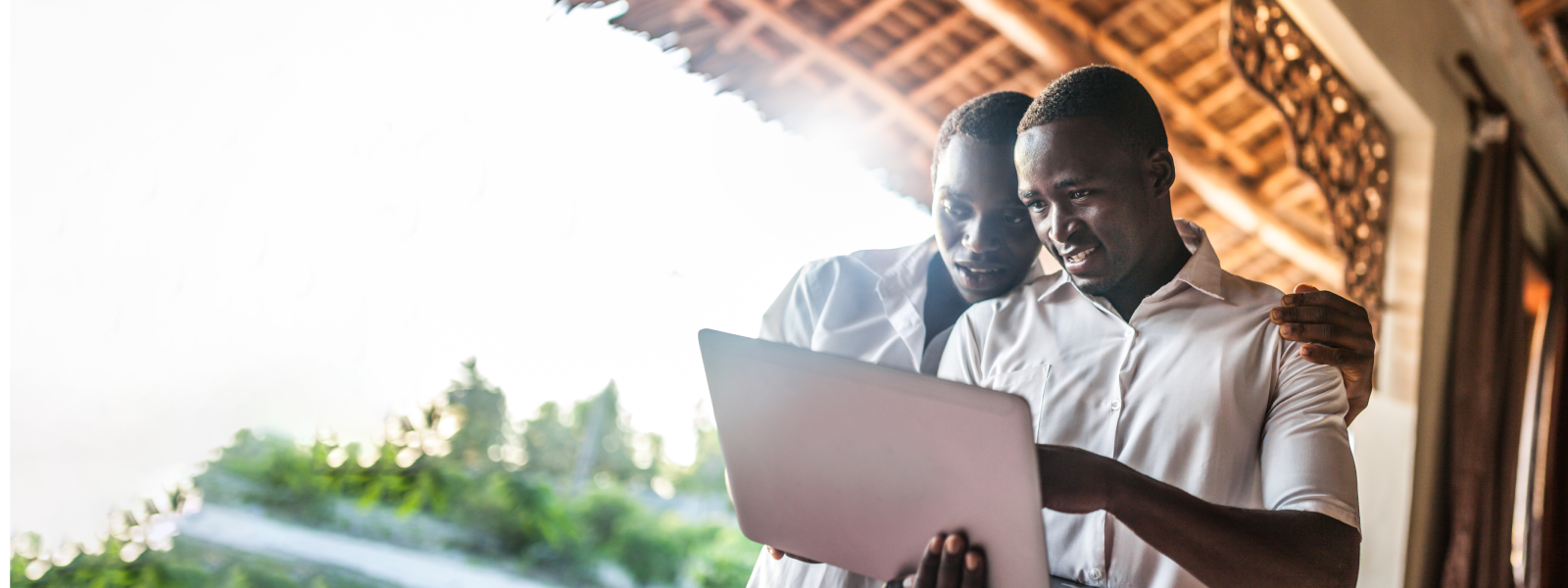 Two young men standing outside viewing a laptop. 