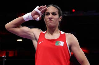 Imane Khelif salutes while wearing a sleeveless athletic top with an Algerian flag emblem during a sporting event