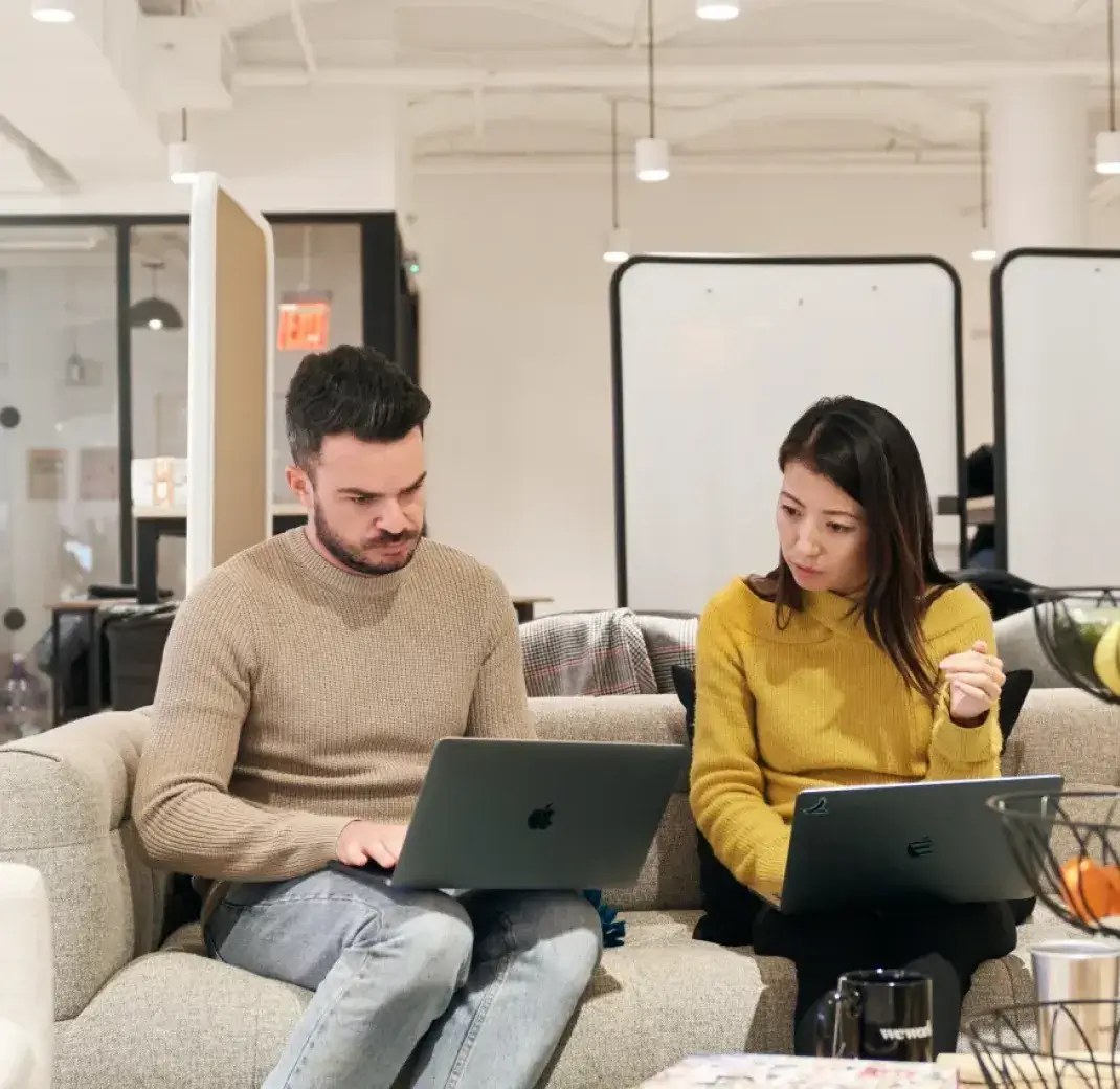 Image of two people sitting on a couch with their laptops and working