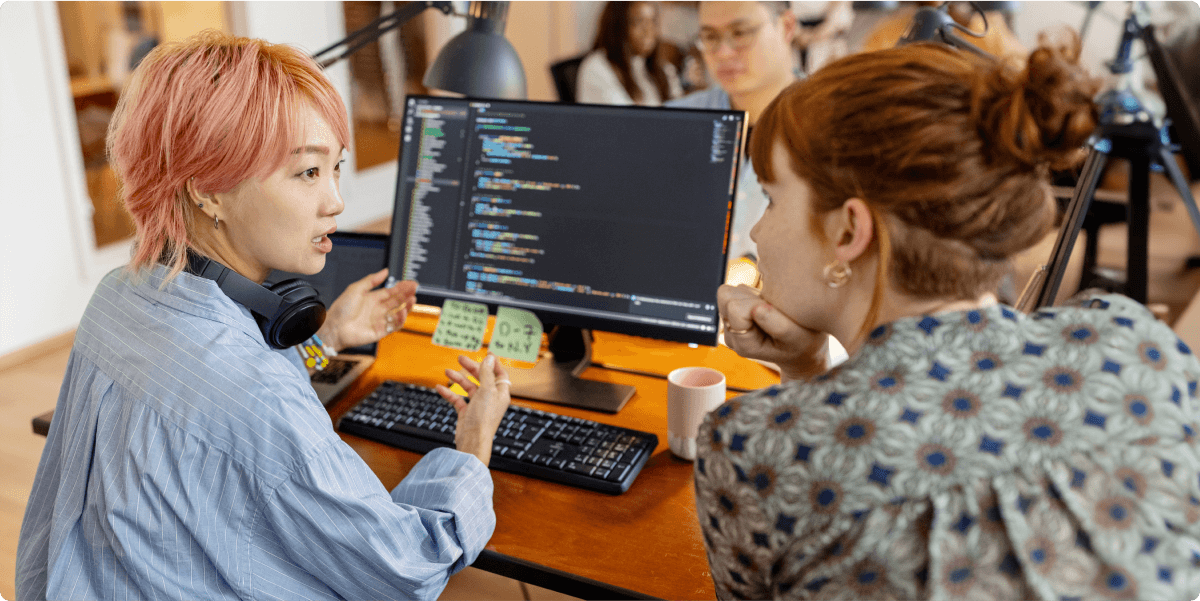 Dos mujeres discutiendo una pregunta de programación en una oficina.