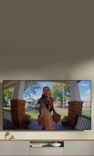 A TV in a living room showing a delivery person standing on a stoop waving to the doorbell camera.