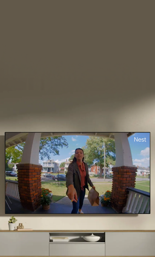 A TV in a living room showing a delivery person standing on a stoop waving to the doorbell camera.