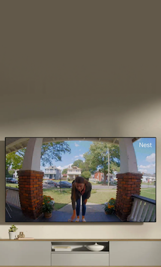 A TV in a living room showing a delivery person standing on a stoop waving to the doorbell camera.