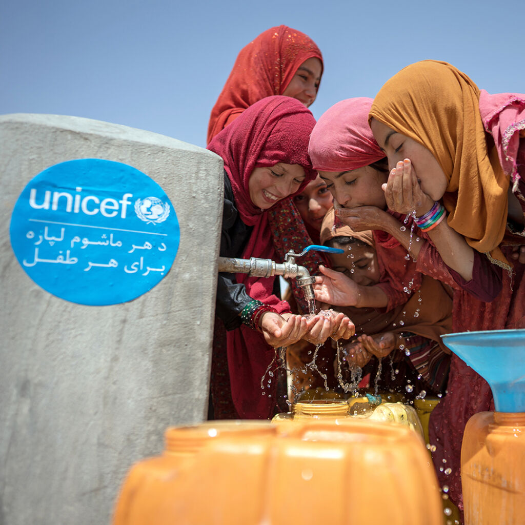 Joukko iloisia lapsia juo vettä UNICEFin pystyttämästä hanasta. 