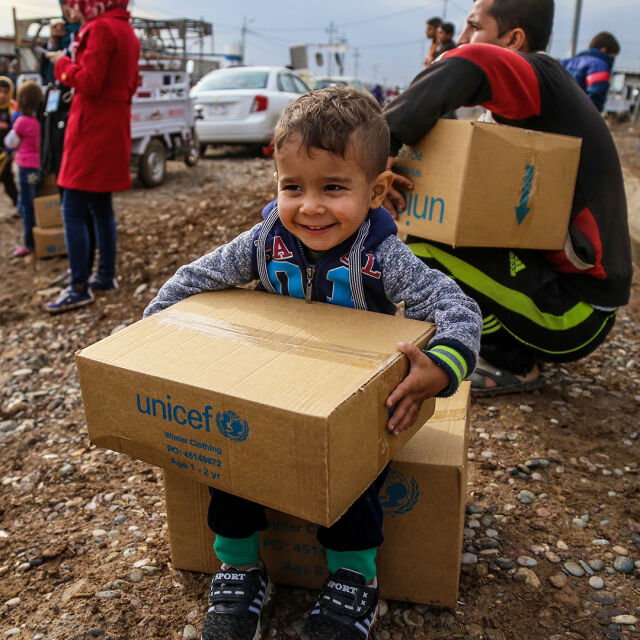 Lapsi istuu ja pitää käsissään pakettia, jossa on UNICEFin logo.