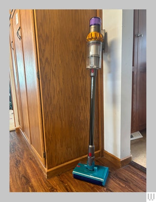 Front view of handheld vacuum with teal base narrow black handle and clear container toward the top