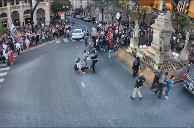 Photojournalist Susan Stava, at center with black backpack, is seen falling to the ground after being shoved while reporting on protests outside a Trump campaign event in Lancaster, Pennsylvania, on Oct. 20, 2024. Her camera lens was damaged in the fall.