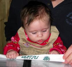 A picture of Carolyn sitting in Eric's laps and gripping a pair of chopsticks in her hand as she looks down at the open menu in front of her.