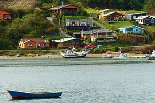 Four boats in Río la Chacra in the foreground and a cluster of small houses on a steep hill in the background