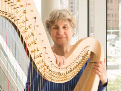 Harpist JoAnn Turovsky looking into the camera next to her instrument.