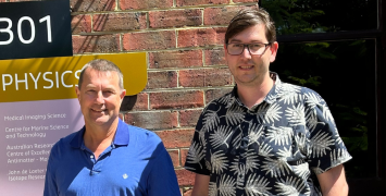 Two men standing side by side in front of a brick wall. 