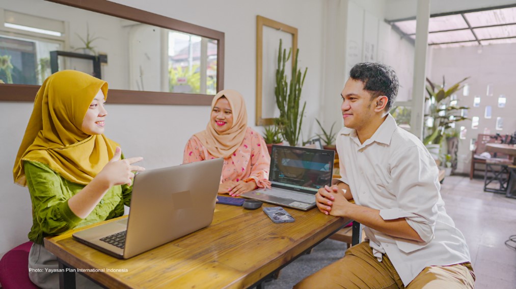 Two women and a man sitting a table with laptops