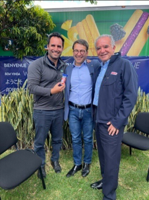 Three men embrace and smile for a photo. 