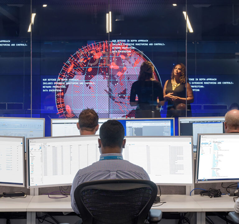 Two people presenting in front of a room with people working on desktop computers