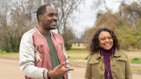 A man and a woman laugh together as they stand outside a vacant lot