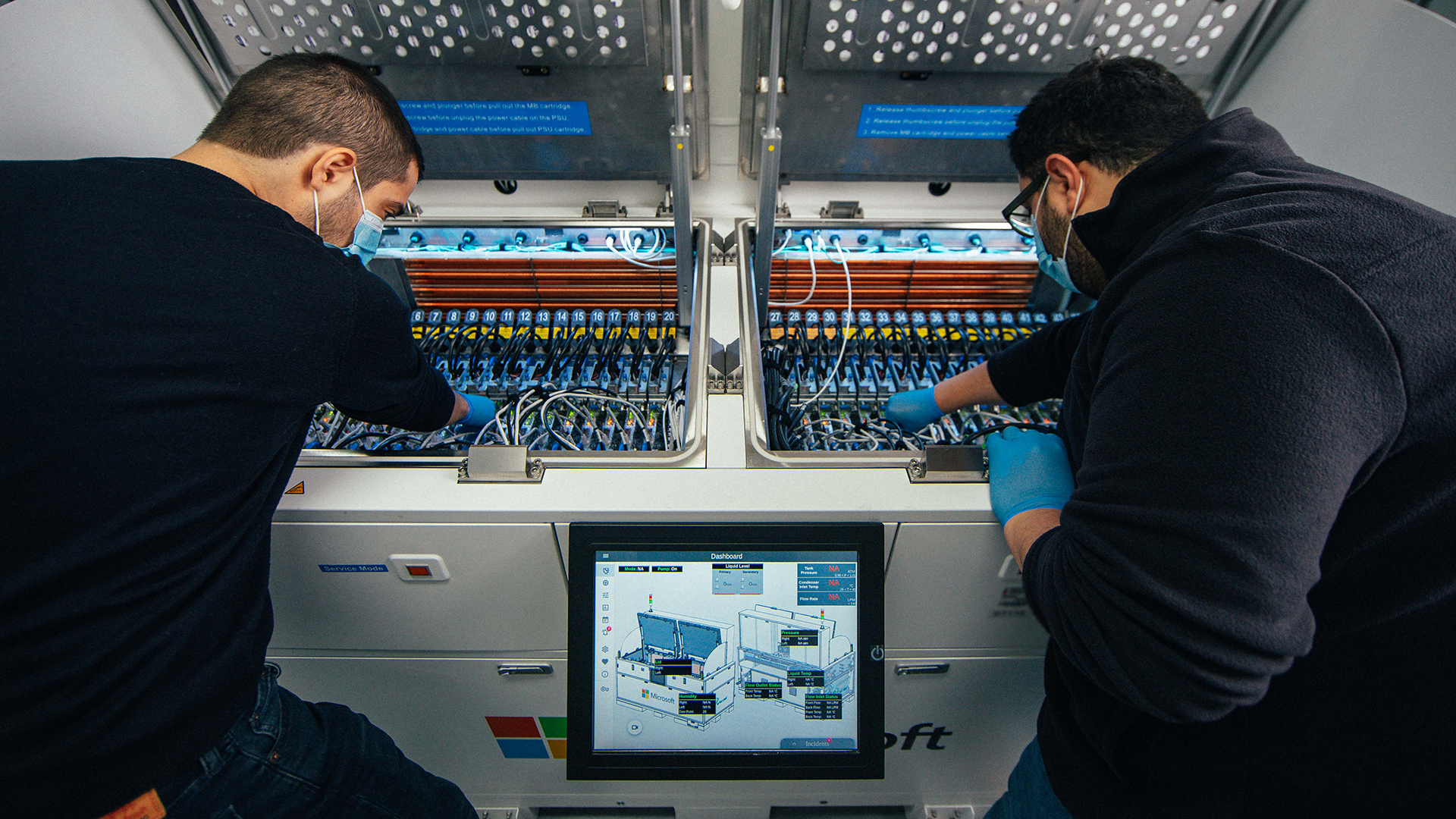 Two men reach into an immersion cooling tank to work on server blades