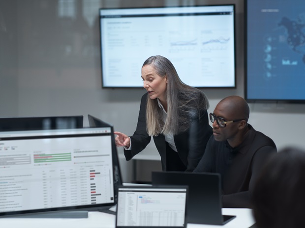 Two employees working amongst computers displaying charts and dashboards