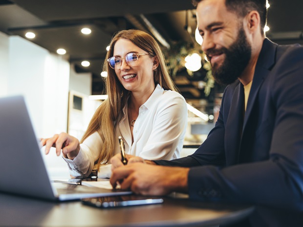 Two coworkers looking happily at a laptop screen in modern office.