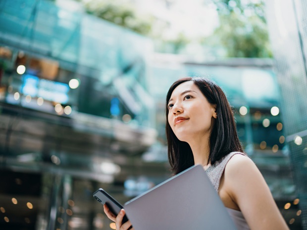 A businesswoman carries a smart phone and laptop on her commute to work in central business district.