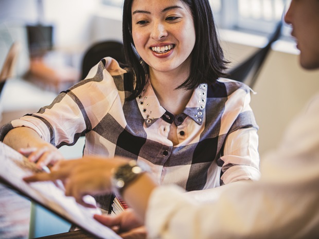 Woman smiling and gesturing to her computer screen while talking to a colleague who is out of frame