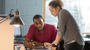 Two people leaning over a desk in conversation