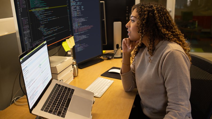 Technology professional sitting in front of two large monitors and a laptop on a stand