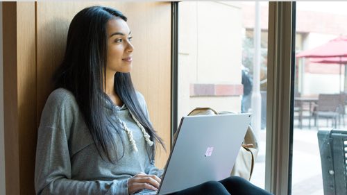 Person sitting agaisnt a wall holding a laptop looking out a window