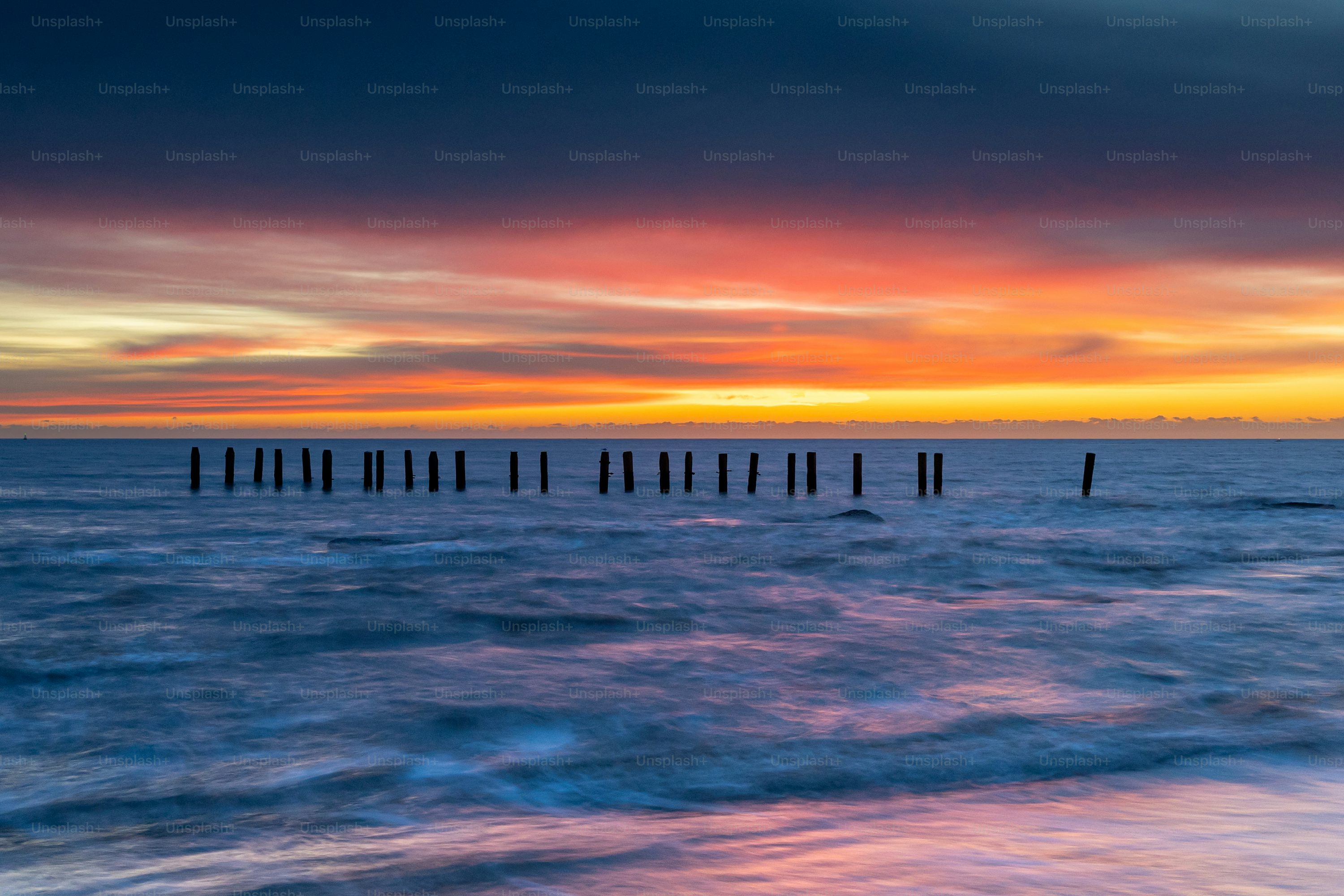 A sunset over a body of water with wooden posts sticking out of the water