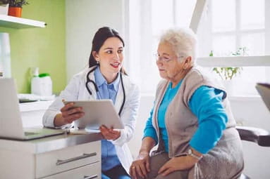 Young, white female doctor consulting her senior, white female patient in an exam room.