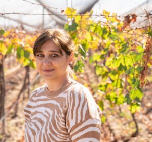 A woman smiles while standing in a vineyard