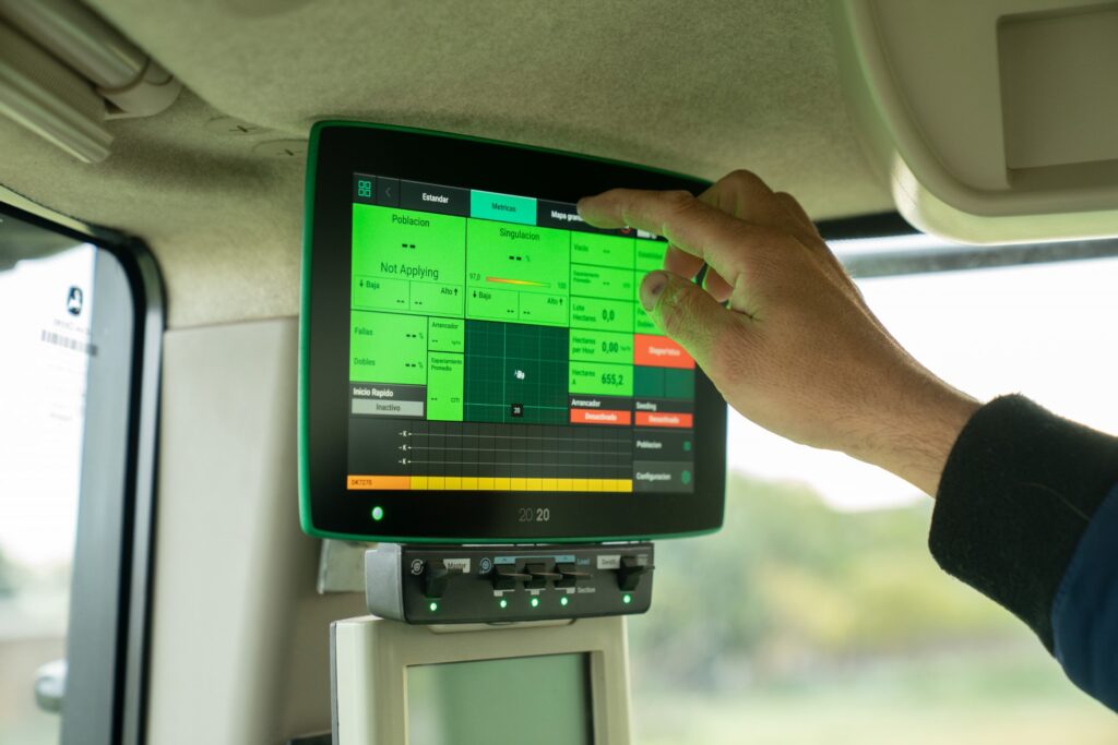 A man’s hand points at a digital platform on a screen mounted in a tractor