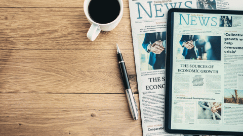 a newspaper and a tablet showing the same news page