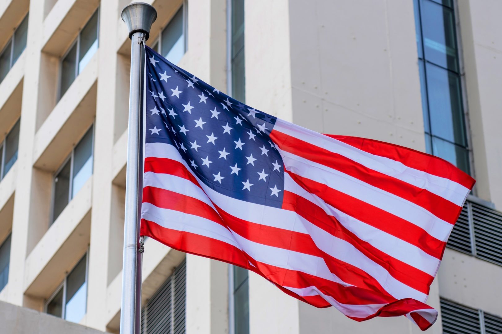 An American flag waving on a flagpole in front of a modern building facade.