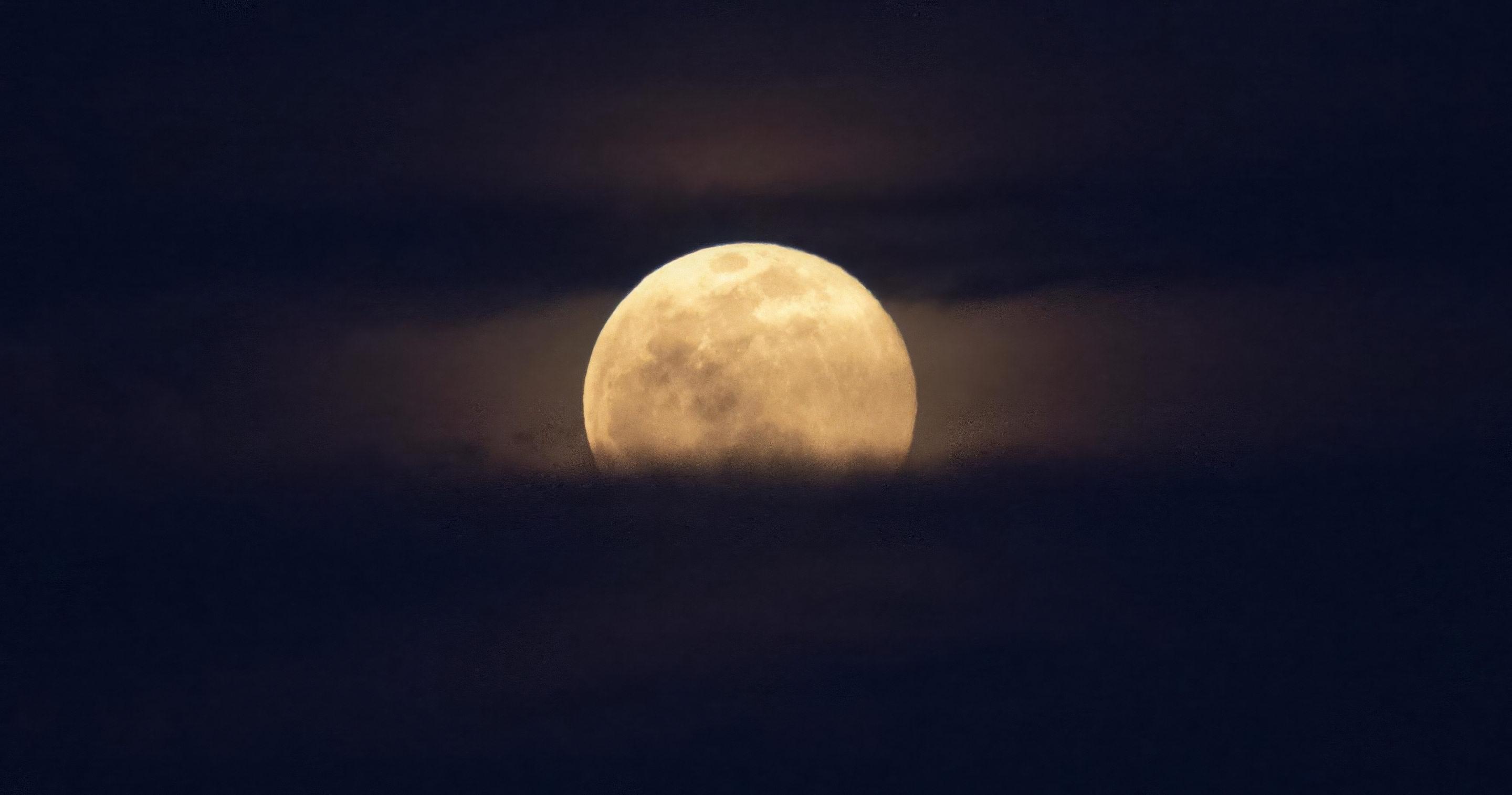 A full moon rises over a bank of clouds in the night sky.