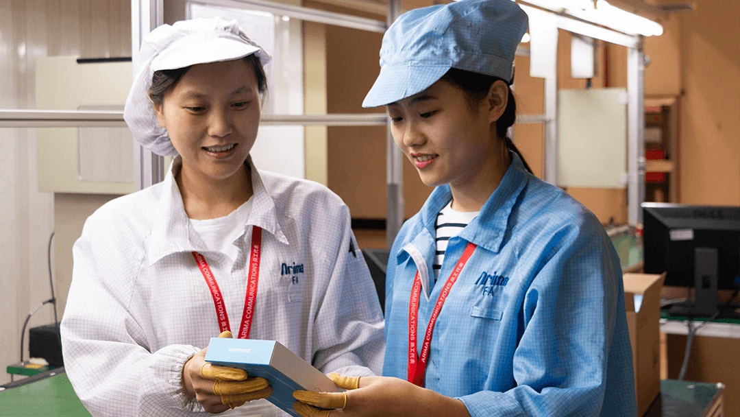 Two Asian women engineers in a tech manufacturing facility, one in a white lab coat and the other in a blue work shirt, examining a Fairphone box, symbolizing the brand's commitment to transparency and ethical production practices.