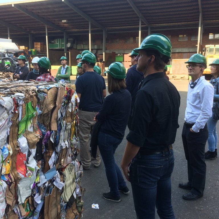 Teilnehmende stehen auf einem Recyclinghof vor gepressten Ballen